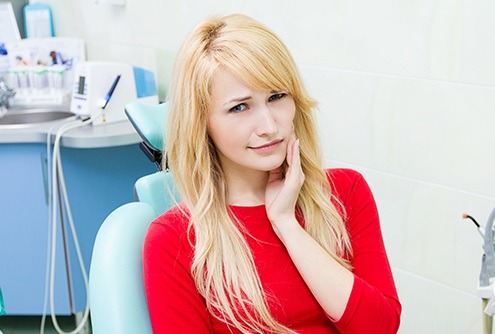 Woman in dental chair holding cheek