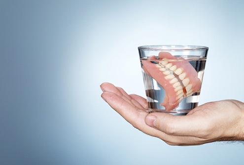 a person holding a glass of water with dentures soaking in them