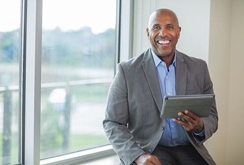 A middle-aged man holding a tablet and showing off his new smile that contains dental implants