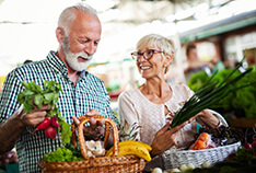 An older couple smiling while at the market buying vegetables