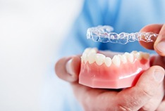 A dentist holding a mouth mold with crooked teeth and preparing to place an Invisalign aligner over the top of the lower arch in McMinnville