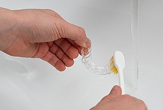 Patient using toothbrush to clean aligner