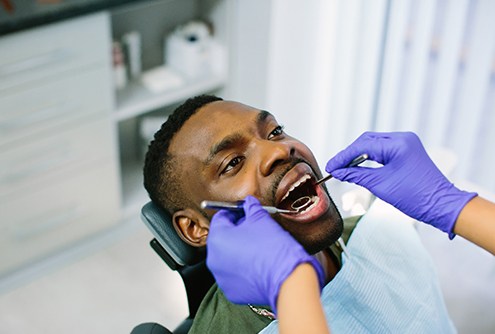 A dentist examining a male patient’s mouth in preparation for creating a treatment plan for a smile makeover 