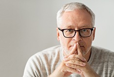 Man with grey hair with his fingers on his lips thinking