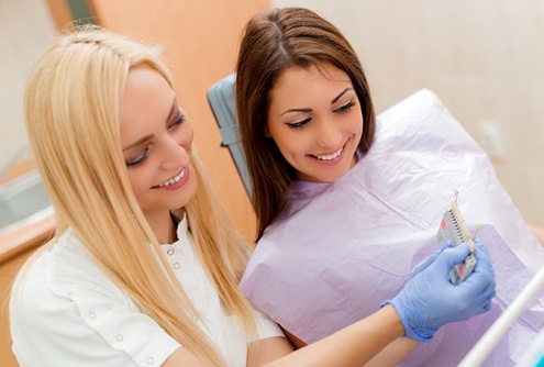 A dentist using a shade guide while talking to a female patient