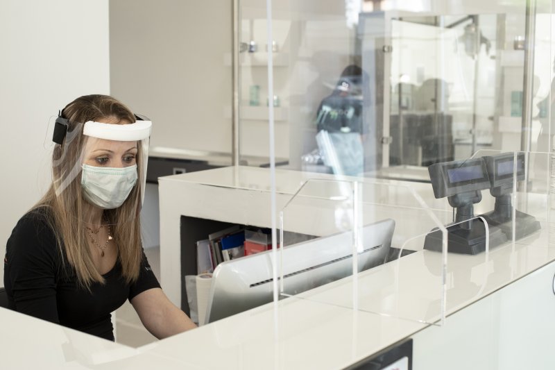 a dentist in McMinnville wearing a face mask and shield seated behind a glass barrier