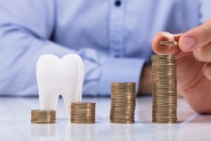 Model tooth and piles of coins demonstrate cost of dental implants in McMinnville