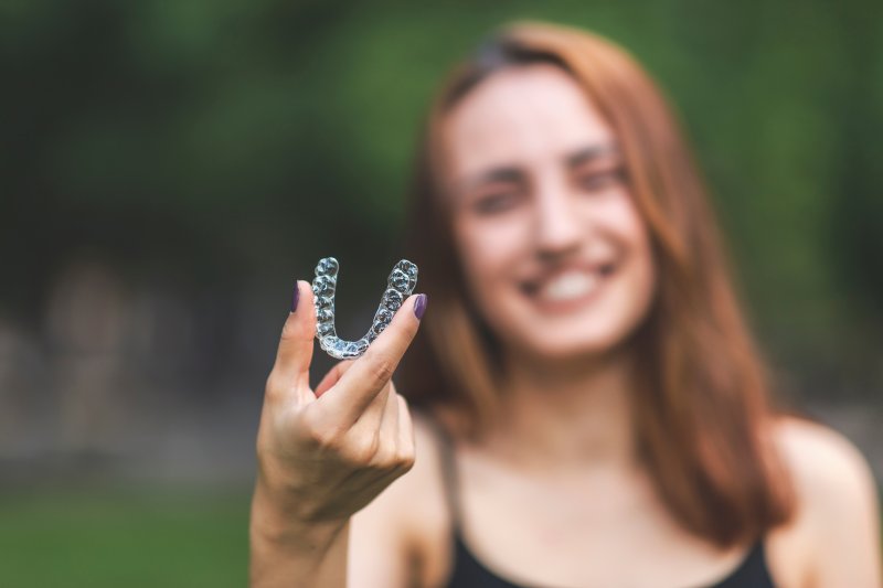 person holding Invisalign aligner and smiling