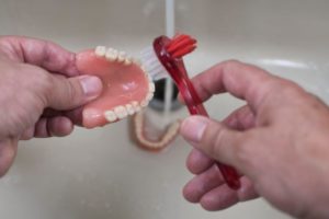a person brushing their dentures  over a sink