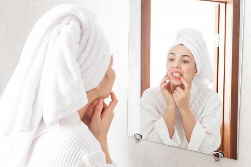 A woman checking her teeth in a bathroom mirror while wearing a bath robe